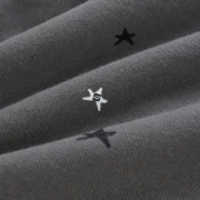 Close-up of the grey Sp5der Splat Punk Hoodie fabric featuring scattered star print graphic branding details.