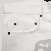 Close-up view of the Sp5der V3 logo on the white denim shorts from the SS25 collection, highlighting hardware details.