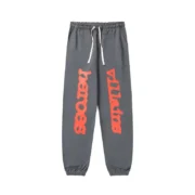 Front view of the grey Sp5der x Heroes and Villains unisex sweatpants featuring vibrant red graphic text on legs.