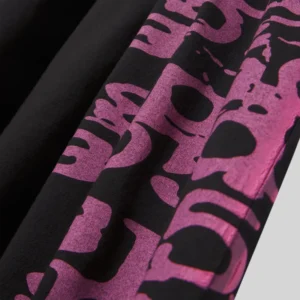 A detailed close up view of the black Sp5der Stacked Tee featuring bold purple graphic lettering on fabric texture.