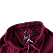 Close-up view of the elastic waistband and tag detail on the SP5DER Nocturnal Highway cotton track pants in maroon.