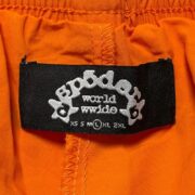 Close-up view of the black neck label on orange Sp5der OG Web Double Layer Shorts featuring branding detail.