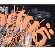 Close-up view of the bold orange graphic design on the SP5DER x Cactus Jack x ComplexCon exclusive black streetwear tee.