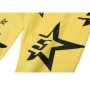 A close-up view of the bright yellow Sp5der 5Star sweatpants featuring a bold black star print streetwear graphic.