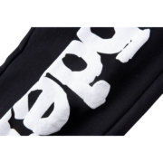 Close-up view of the Sp5der Souvenir SP5 Sweatpants featuring a distressed white graphic brand logo on black fabric.