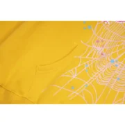 Front detail view of the vibrant mustard-yellow Sp5der P*NK collaboration hoodie with signature web graphic print.