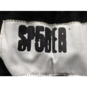 Detailed close-up view of the branded Sp5der logo tag stitched on the black Sp5der Sex AOP streetwear sweatpants.