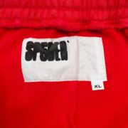 Close up of the Sp5der OG logo tag on premium red streetwear sweatshorts featuring an XL size label for authenticity.