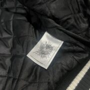Close-up of the official inner brand label inside the black quilted lining of a SP5DER Division 5 Varsity Jacket.
