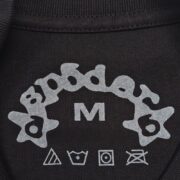 Close-up of the Sp5der Warped Tee black inner neck label detail featuring brand logo and size medium tag.
