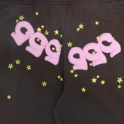 Detail view of black Sp5der 555 555 sweatpants featuring pink iconic lettering and small yellow star graphics.