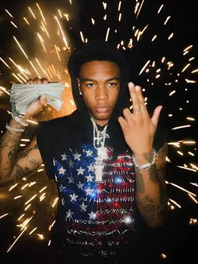 Man wearing a Sp5der USA flag graphic hoodie in a lifestyle shot featuring bright fireworks and cash in hand