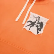 Close-up view of the orange Sp5der 5Star Rodeo hoodie featuring a distressed patch graphic detail on the chest