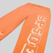 A close-up of the vibrant orange Sp5der 5Star Rodeo sweatpants featuring the signature SP5DER leg text print design.