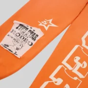 Close-up view of the Orange Sp5der 5Star Rodeo sweatpants featuring the signature distressed graphic patch design.