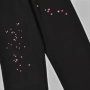 Close-up view of Sp5der Black Angel Number sweatpants featuring iconic pink star print graphics on premium cotton fleece.