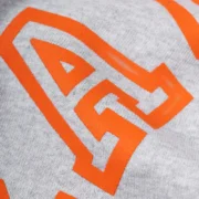 Close-up view of the orange graphic print on the heather grey Sp5der Arach sweatpants premium fleece fabric.