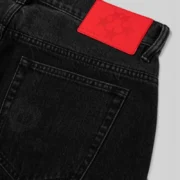 Close-up of Sp5der Beluga Black Wash denim pants highlighting the signature branded red leather back patch detail.