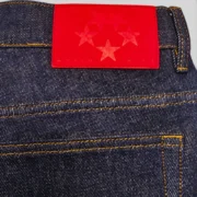 Close-up view of the Sp5der Beluga Denim Indigo jeans showing the signature red leather patch with star graphic.