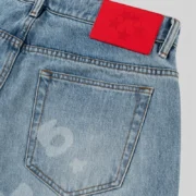 Close-up of Sp5der Beluga Denim Light Blue Wash jeans featuring a distinctive red patch on the back waistband.