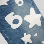 Close-up of Sp5der Beluga Wash Denim in Light Indigo featuring the prominent white 5Star graphic print on the fabric.