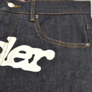 Close up view of the Sp5der V3 Indigo Denim jeans showcasing the waist area and front graphic branding detail.