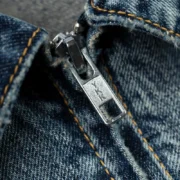 Close-up view of the metallic YKK zipper detail on the Sp5der Light Blue Wash denim work jacket with frayed edges.