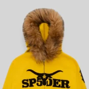 Close-up of the yellow Sp5der zip-up hoodie featuring a plush faux fur hood trim and black Sp5der logo branding.