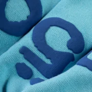 Close-up view of the dark blue signature puff print detailing on the light blue Sp5der OG Web V2 spray sweatpant.