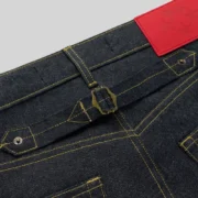 Close-up of Sp5der Punk V3 Logo Indigo Denim Jeans featuring an adjustable back waist buckle and red branding patch.
