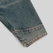 Close-up view of the sleeve on the Sp5der Script Denim Work Jacket in a vintage-style light wash denim finish.