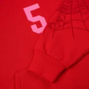 Close-up of the red Sp5der Stadium hoodie featuring the signature pink '5' graphic and sleeve web print details.