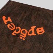 Close-up view of the Sp5der T&F Tree Camo Brown sweatpants featuring the iconic orange puff print logo detail.