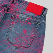 Detailed close-up of Sp5der V2 Web Denim Indigo jeans featuring pink all-over web graphics and red leather label.