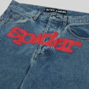 Detailed close-up of the front graphic on the Sp5der V3 Indigo Denim jeans in a light wash finish with red branding.