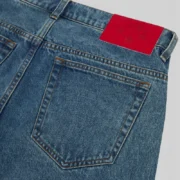 Close-up view of the back waistband leather patch on Sp5der V3 Indigo Denim Light Wash jeans in classic streetwear style.